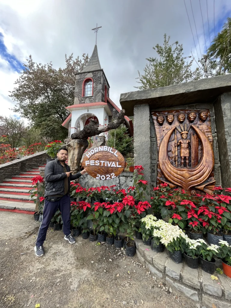 Man posing near Hornbill Festival signboard and sculpture